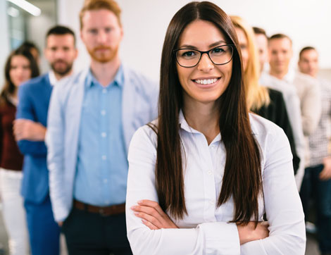 A smiling businesswoman stands confidently with her team in a modern office, showcasing positive corporate culture.