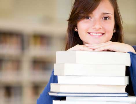 A smiling woman rests her chin on a tall stack of books, representing vet training.