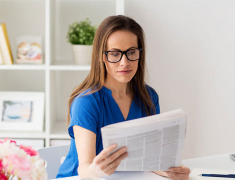 VET Sector News | CAQA Publications A woman reads a newspaper while working from home, featuring VET sector news.